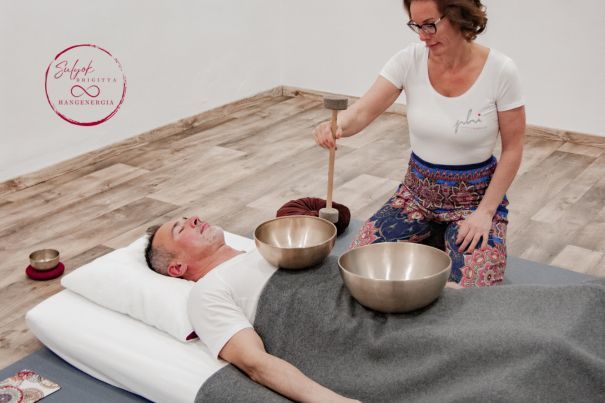 Sulyok Brigitta hangmasszőr-specialista egy világos, üres teremben hangmasszázst végez. Egy szőnyegen térdel, előtte egy nyugodt, relaxált férfi fexik, a testén 2 hangtál van, amiből Brigitta egy ütővel éppen megszólaltatja a kisebbet. A férfi fejénl szintén egy hangtál található egy bordó párnán.